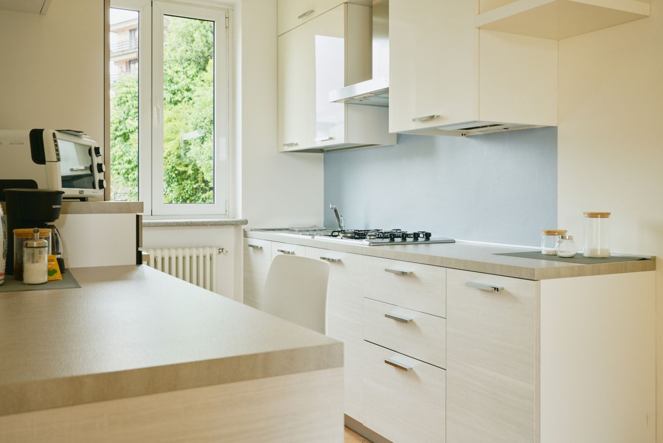 Cocina moderna con armarios blancos, estufa a gas y ventana con vista a zonas verdes.