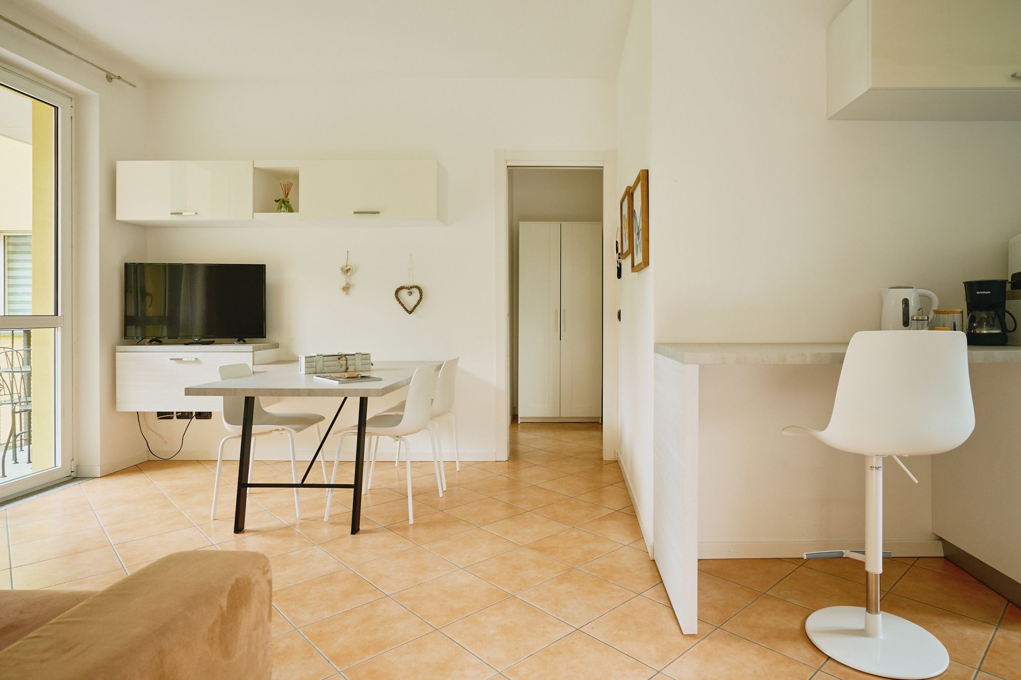 Un salon moderne comprenant un canapé, une table à manger avec des chaises, un téléviseur et un coin cuisine avec une machine à café.