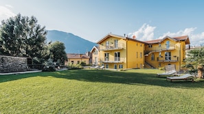 Un edificio giallo a più piani con balconi, un muro in pietra e un prato.