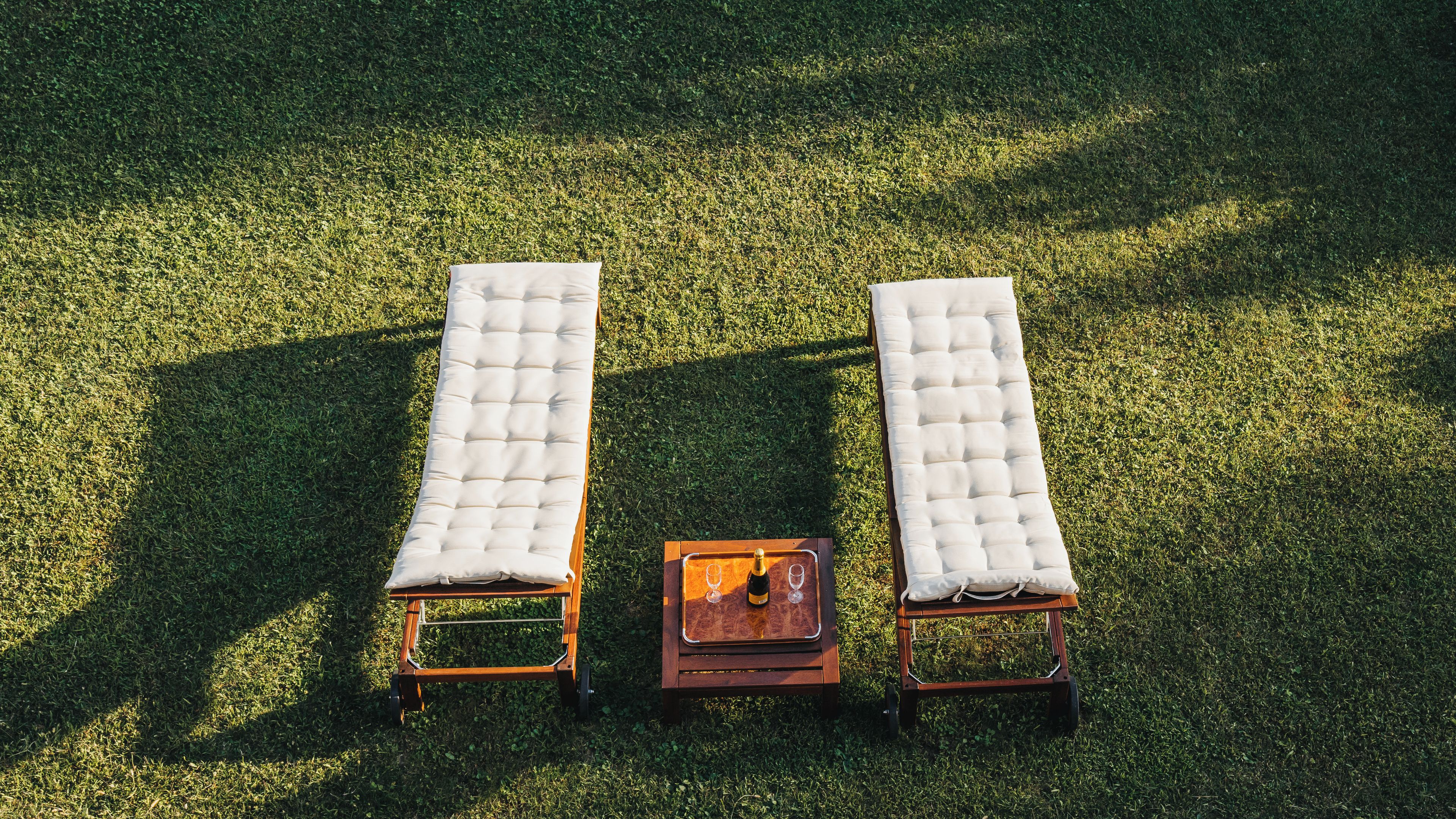 Deux fauteuils de jardin avec des coussins, placés sur une pelouse verdoyante, et une petite table en bois avec une bouteille et des verres au centre.