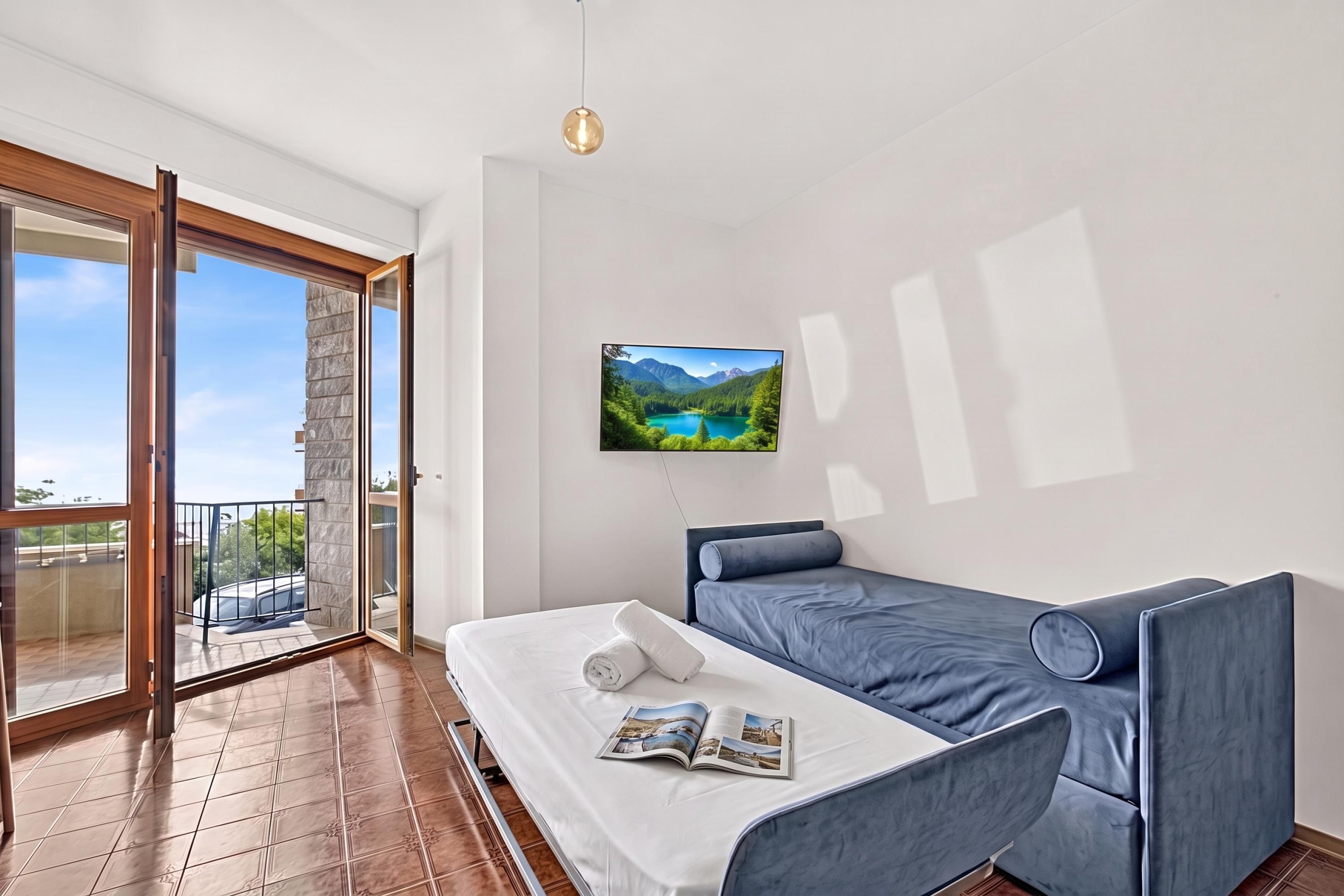 A modern bedroom with a bed, a magazine, and a view of a mountain lake through a window.