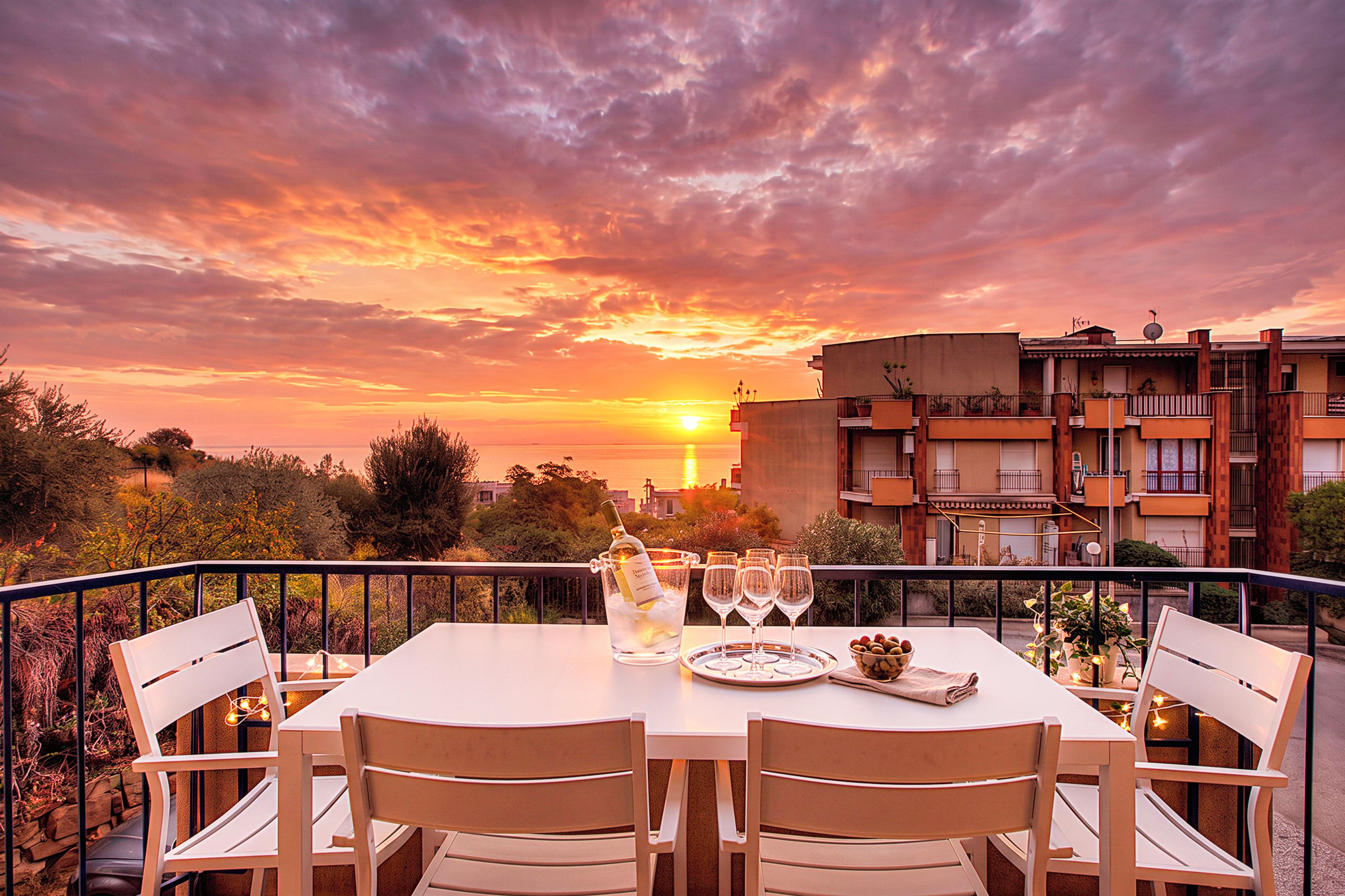 A table set for dining with a sunset view, outdoor seating, and a cityscape in the background.