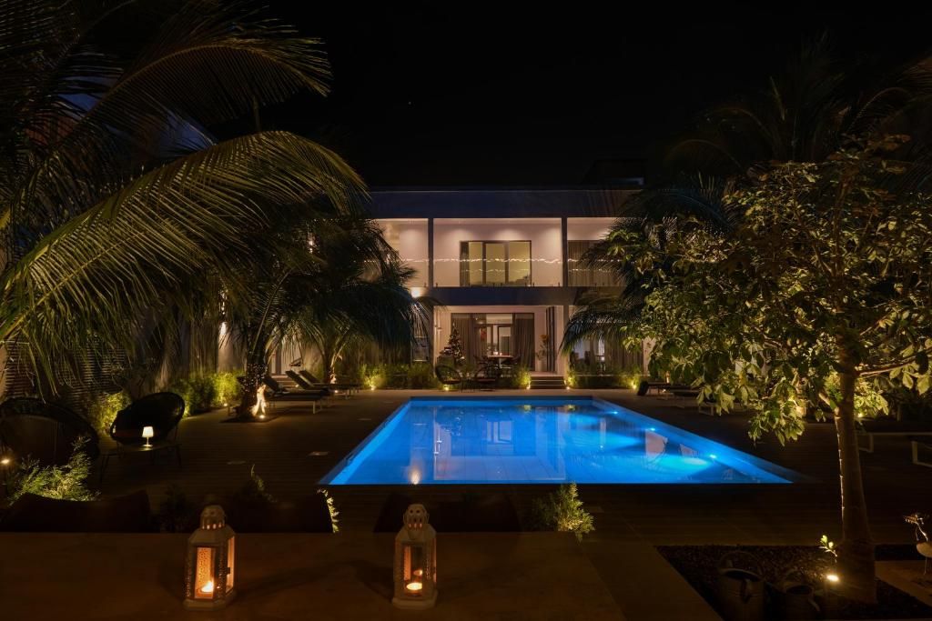 Vista nocturna de un edificio moderno con piscina, rodeado de vegetación tropical.