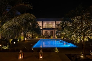 Vista nocturna de un edificio moderno con piscina, rodeado de vegetación tropical.