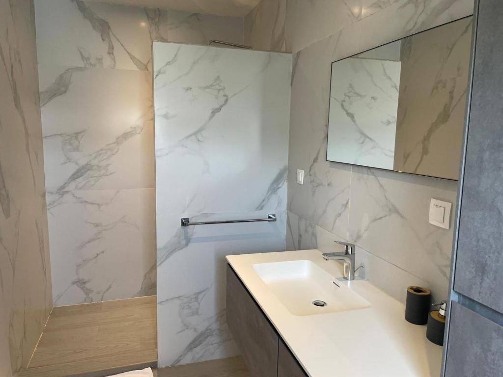 A modern bathroom with a marble wall, a sink, a mirror, and a shower area.