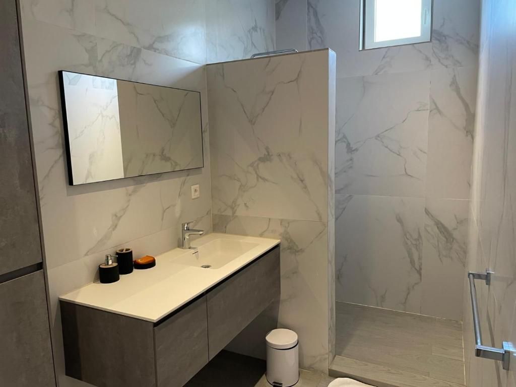 Un baño moderno con salpicadero de mármol, un espejo grande, un lavabo con tocador y una zona de ducha.