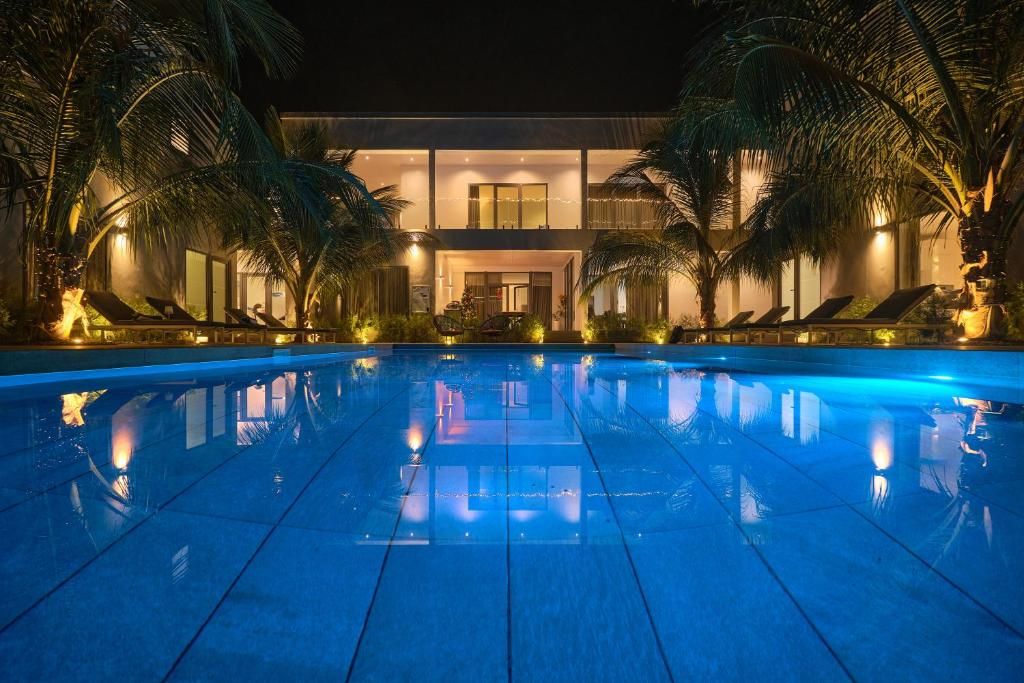 A nighttime view of a hotel with a swimming pool, palm trees, and a two-story building with balconies.