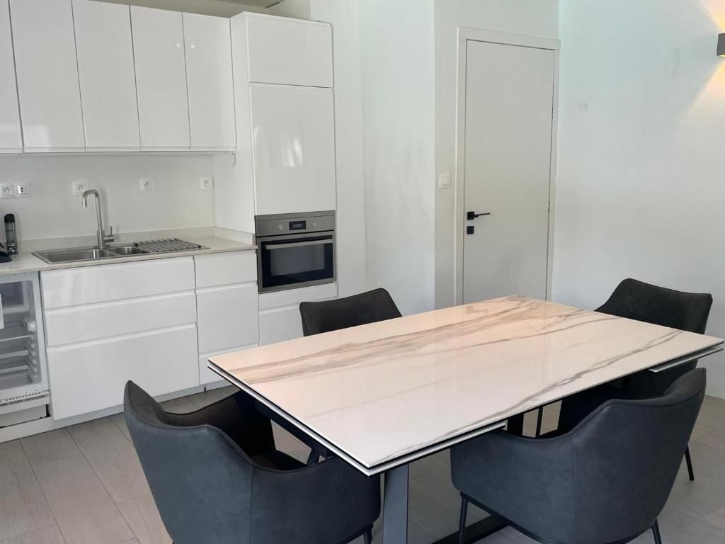 Una cocina moderna con armarios blancos, horno integrado y mesa de comedor con cubierta de mármol y cuatro sillas.