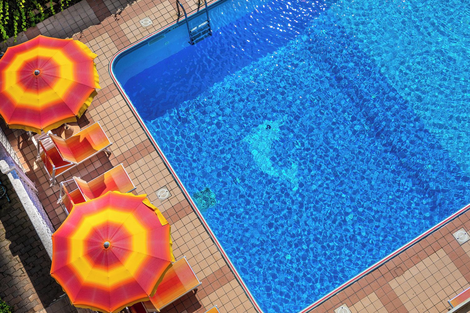 Een zwembad met helderblauw water, omringd door een betegeld zonnedek en voorzien van ligbedden en parasols.