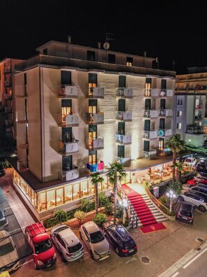 A multi-story hotel with balconies, a covered outdoor seating area, and a parking lot. - Hotel Jalisco (Lido di Jesolo)