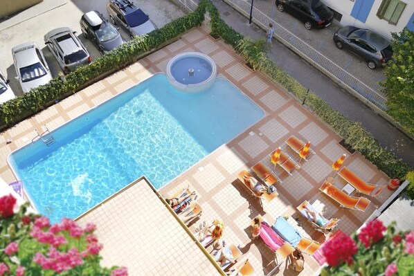 A rooftop pool with a fountain, surrounded by lounge chairs and umbrellas, with cars parked nearby. - Hotel Jalisco (Lido di Jesolo)