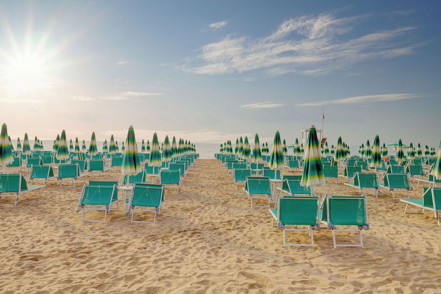 Ein Strand mit Reihen aus grünen Liegestühlen und Sonnenschirmen, die in einem Muster angeordnet sind.