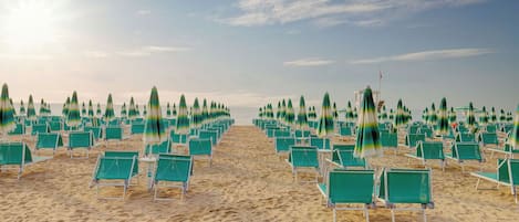 Ein Strand mit Reihen aus grünen Liegestühlen und Sonnenschirmen, die in einem Muster angeordnet sind.