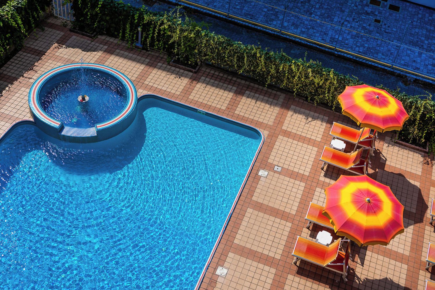 Une piscine avec un jacuzzi, entourée de chaises longues et de parasols.