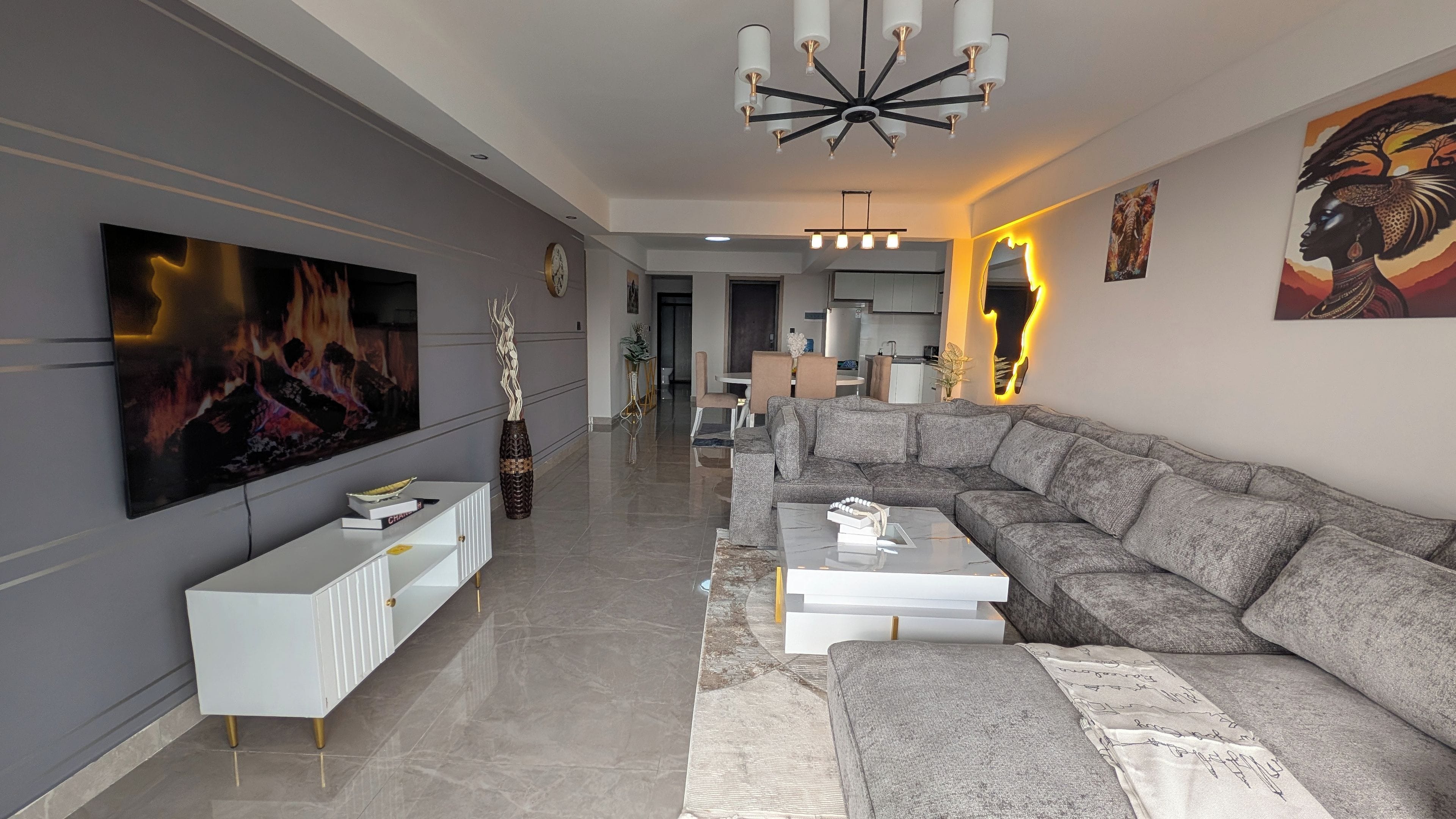 A modern living room with a sectional sofa, a white console table, a flat-screen TV, and decorative wall art.