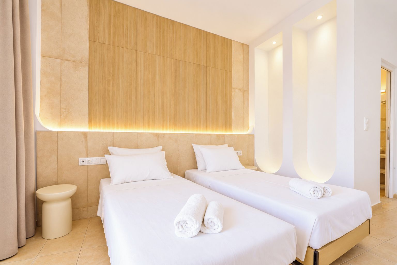Une chambre d’hôtel avec deux lits, une tête de lit en bois, une table de chevet ronde et une porte de salle de bain.