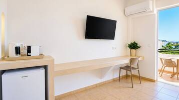 A modern room with a flat-screen TV mounted on the wall, a small kitchenette with a refrigerator, a chair, and a potted plant.