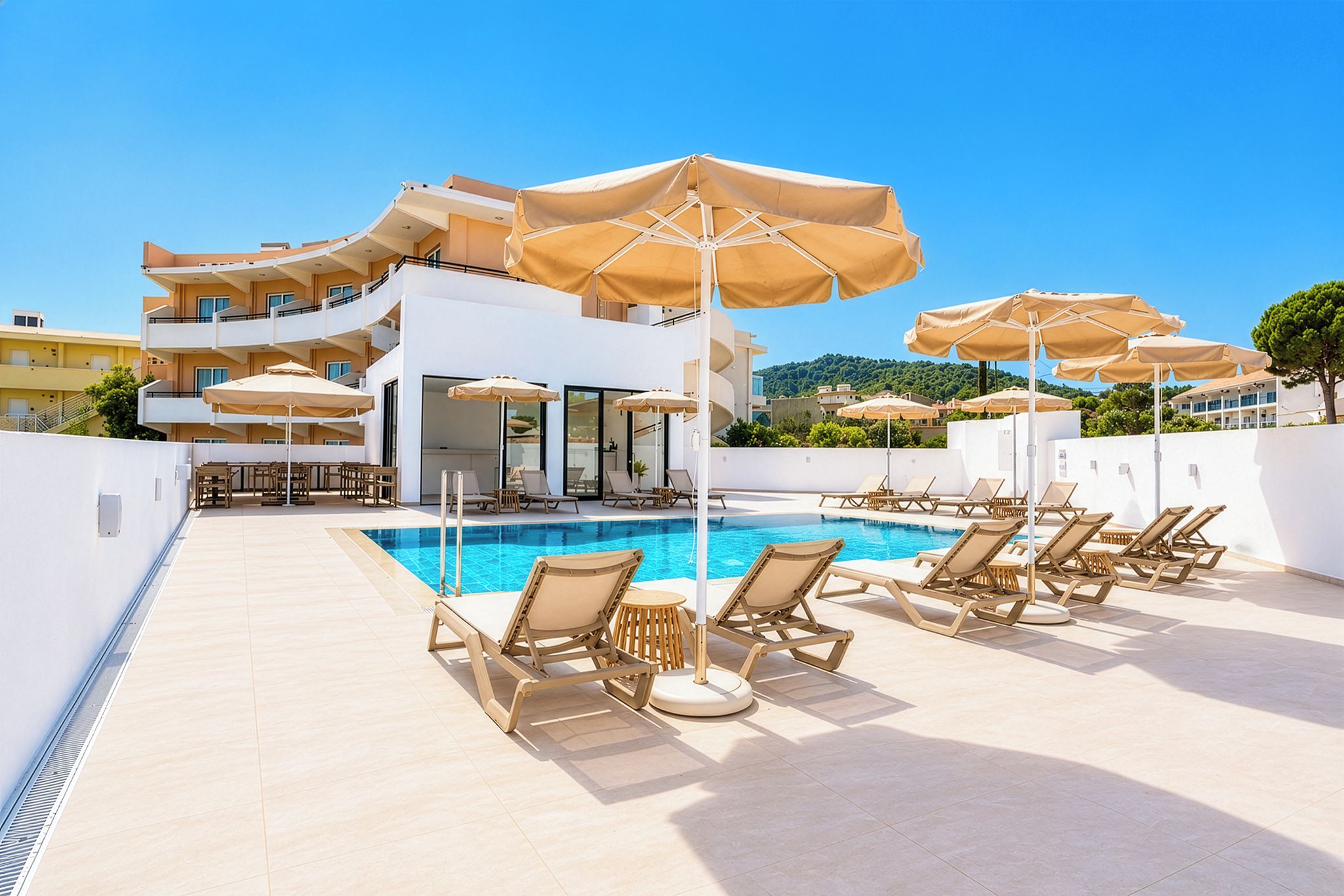 A rooftop pool area with sun loungers and umbrellas, a clear blue sky, and a view of a hillside.