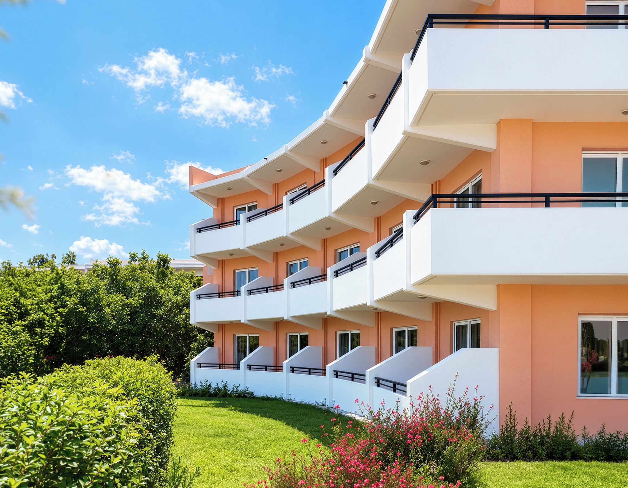 Un edificio residencial de varios pisos con balcones, un césped cuidado y un cielo despejado.