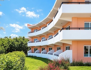 A multi-story residential building with balconies, a well-maintained lawn, and a clear sky.