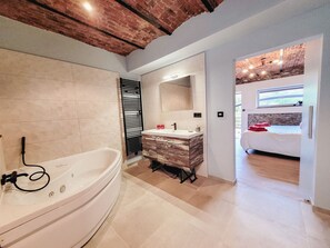 Une salle de bain moderne avec une baignoire sur pieds, un meuble-lavabo avec miroir et un lit dans la pièce adjacente.