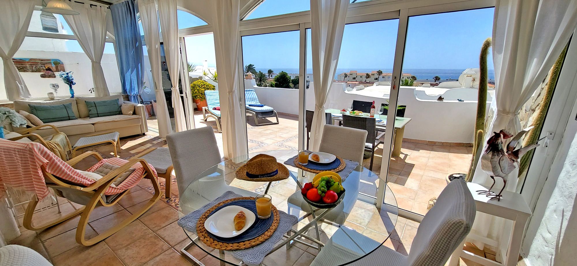A balcony with a table set for breakfast, a sofa, and a view of the sea.