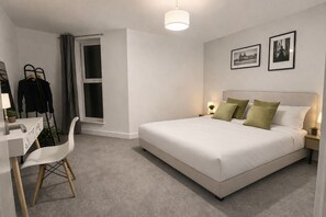 Ein modernes Schlafzimmer mit einem großen Bett, Nachttischlampen, einem Schreibtisch mit Stuhl und einem Fenster mit Vorhängen.