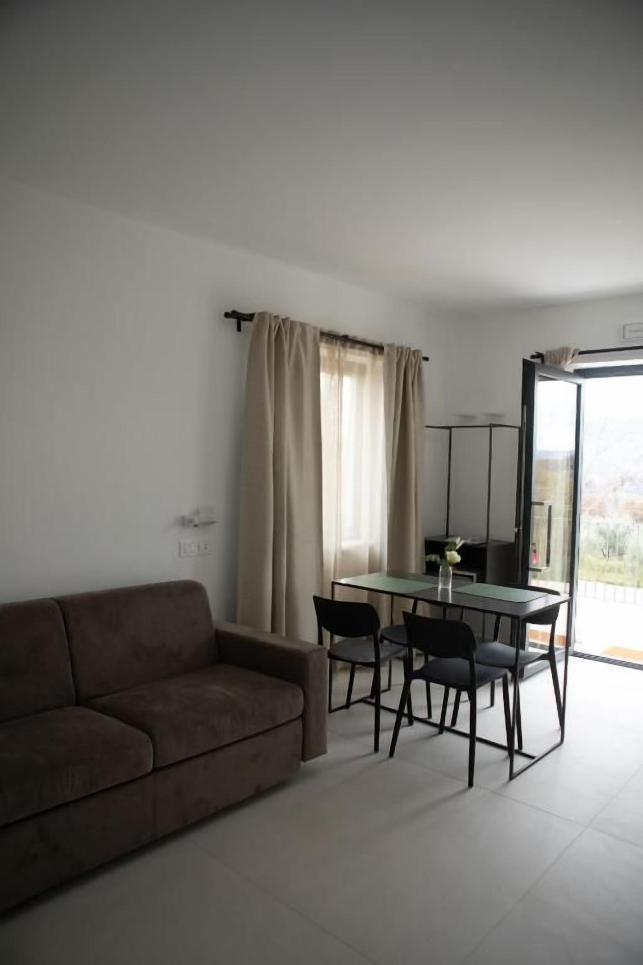 A living room with a sofa, a dining table with chairs, and a view through a glass door.