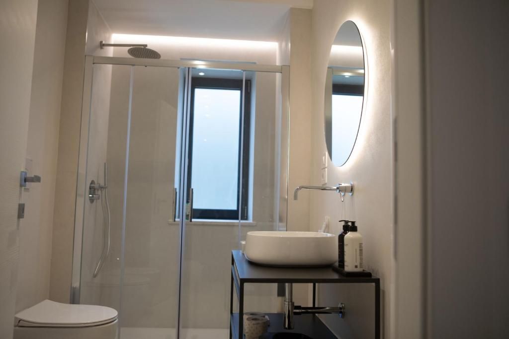 A modern bathroom with a glass-enclosed shower, a toilet, a sink with a mirror, and a window providing natural light.