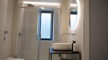 A modern bathroom with a glass-enclosed shower, a toilet, a sink with a mirror, and a window providing natural light.