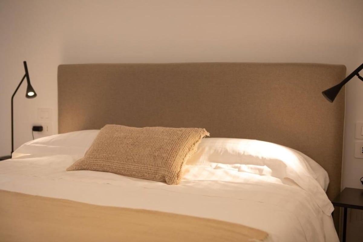 A bed with a beige headboard, a single pillow, and a bedside lamp.