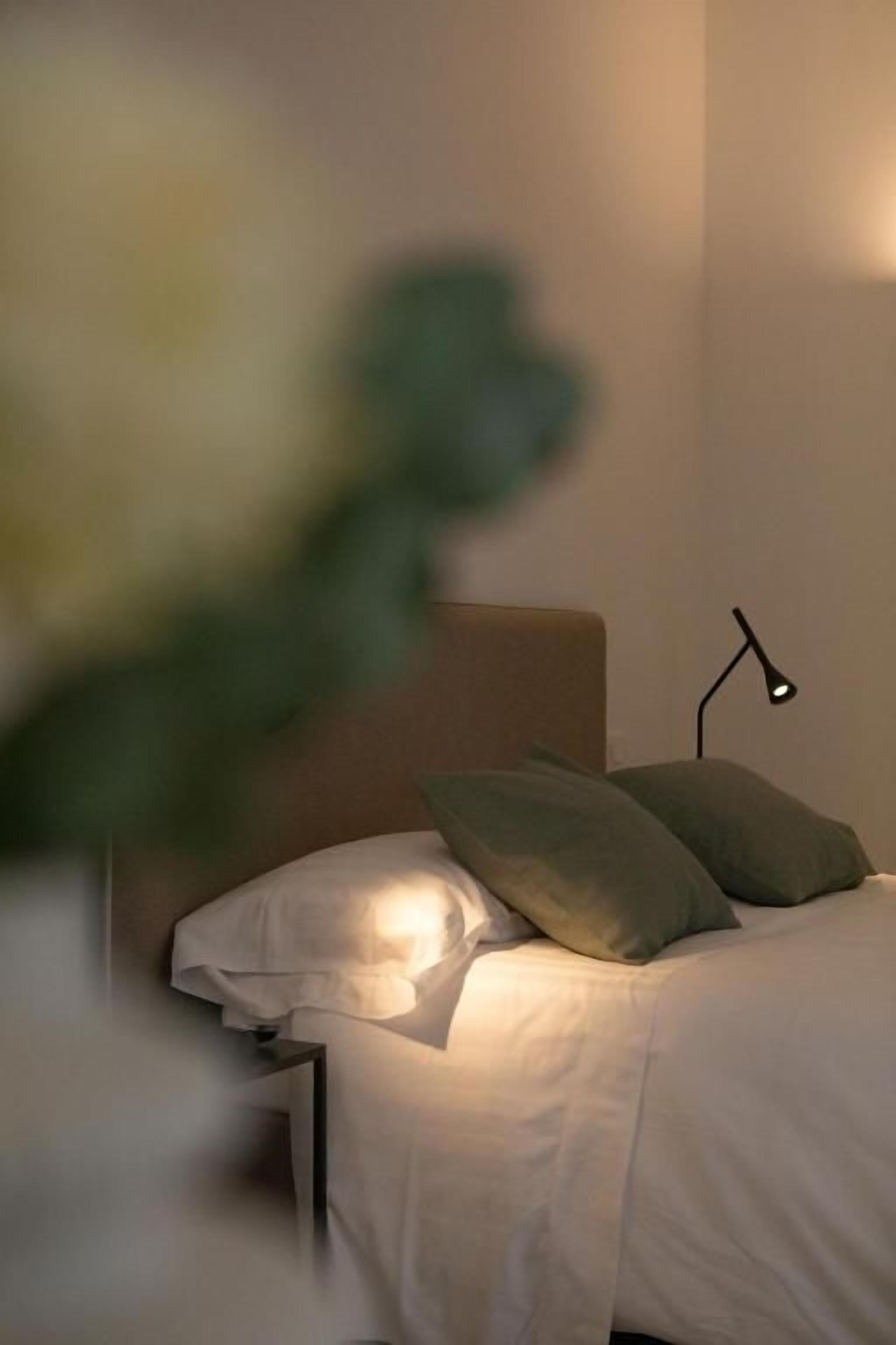 Una cama con almohadas y una lámpara de noche en una habitación con una decoración en tonos neutros.