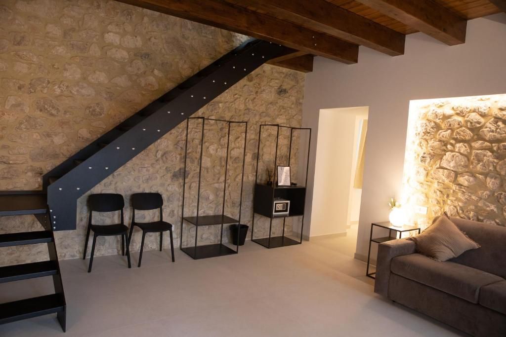 Une pièce avec un mur en pierre, un escalier, un canapé et une petite table avec une lampe.