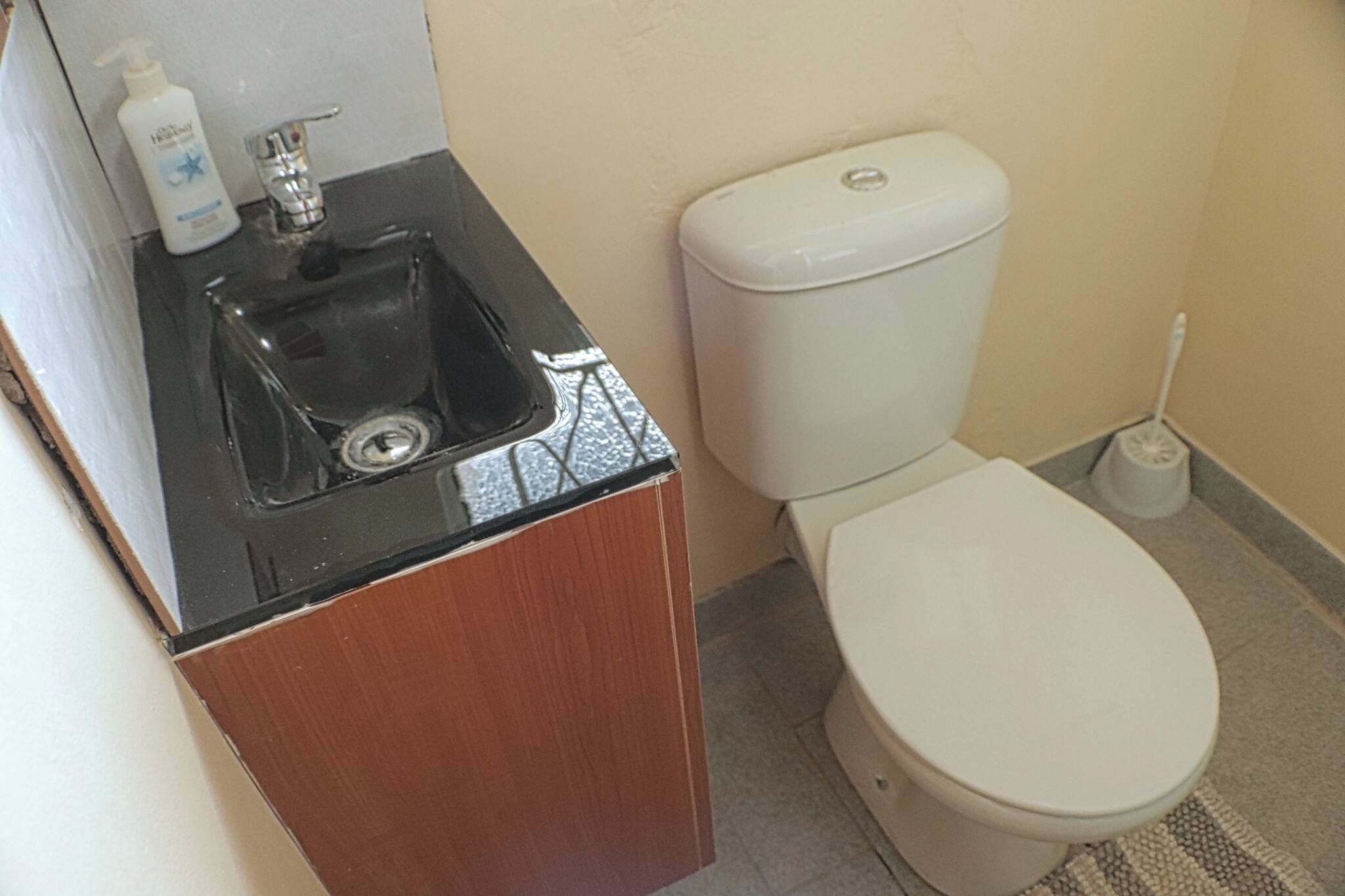 A small bathroom with a sink, toilet, and a toilet brush.