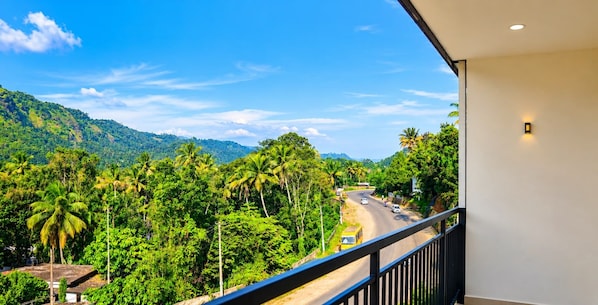 A balcony with a view of a road surrounded by lush greenery and hills.
