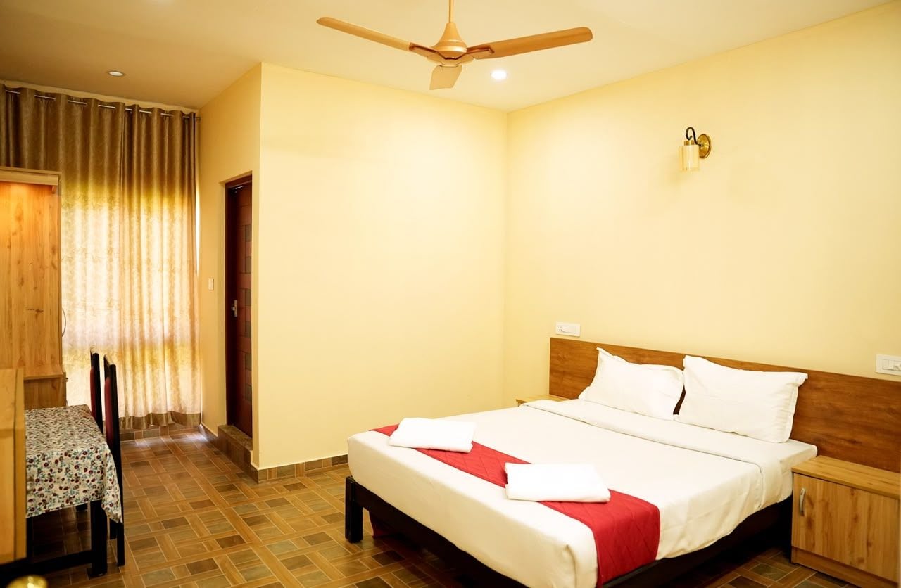 Ein Hotelzimmer mit einem Bett, einem hölzernen Kopfteil, einem Nachttisch, einem Tisch mit Stühlen und einem Deckenventilator.