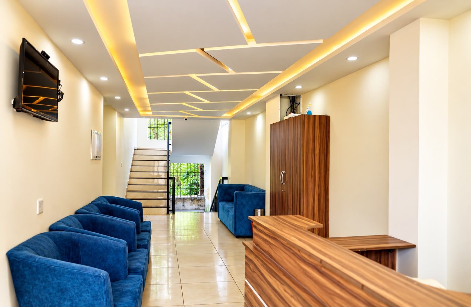 Un vestíbulo de hotel con mostrador de recepción, zona de estar azul y una escalera que conduce a un piso superior.