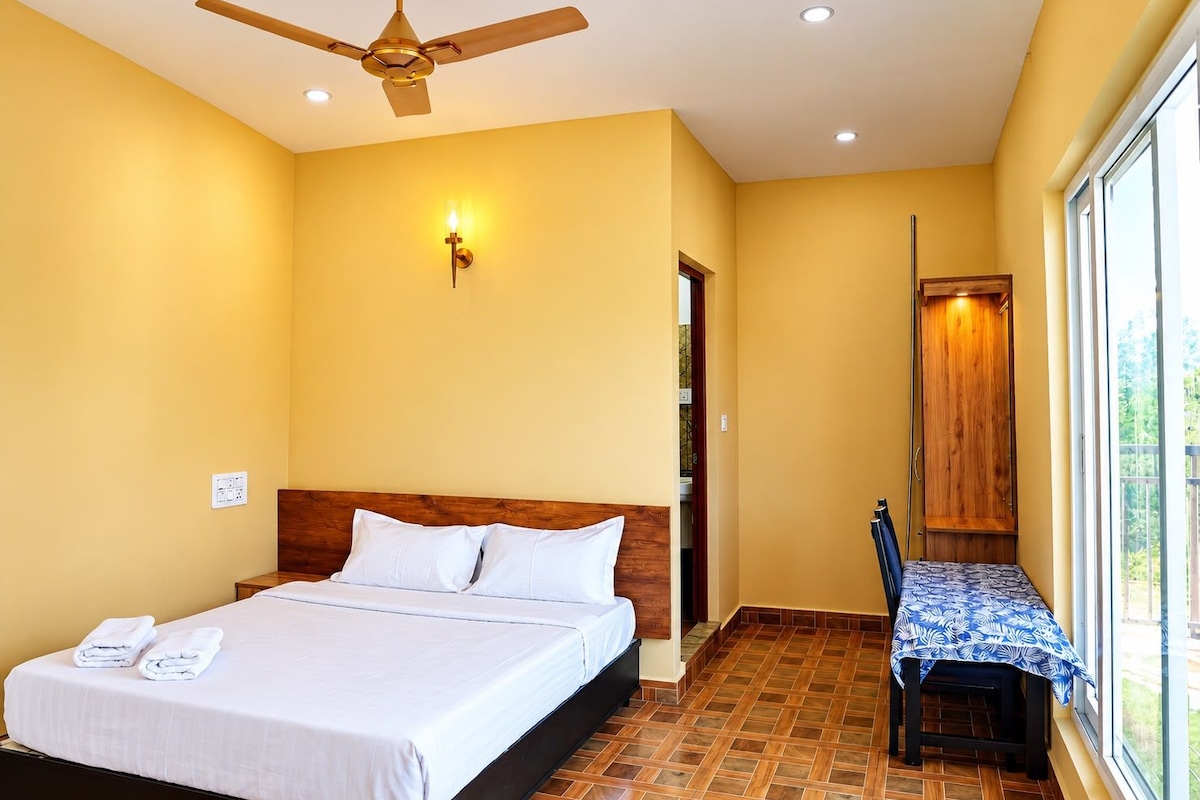 Ein Hotelzimmer mit Bett, Deckenventilator, Wandleuchte, Holztür und Fenster.