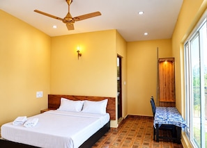 Ein Hotelzimmer mit Bett, Deckenventilator, Wandleuchte, Holztür und Fenster.