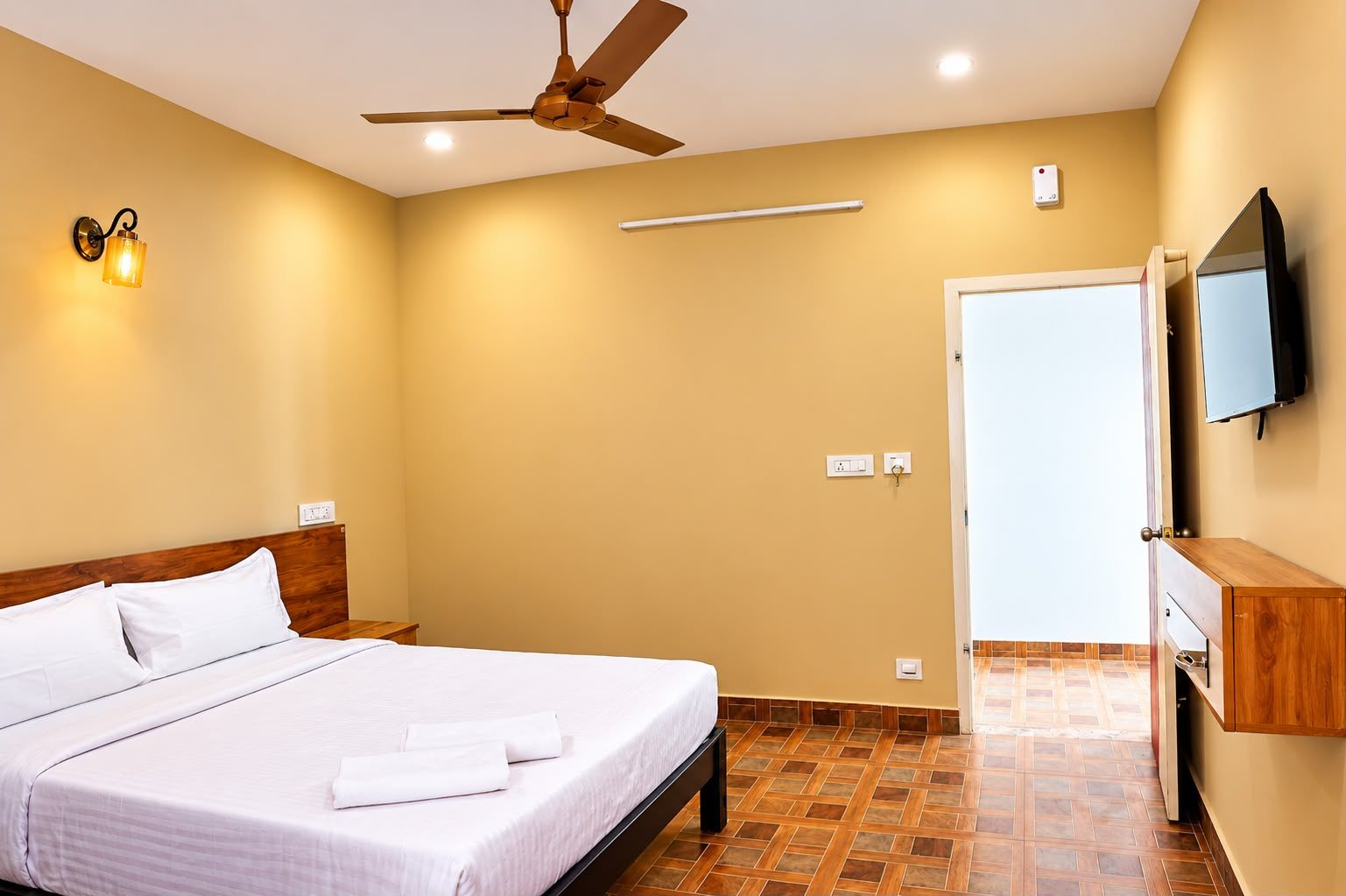 Una habitación de hotel con cama, ventilador de techo, televisor montado en la pared y un armario de madera.