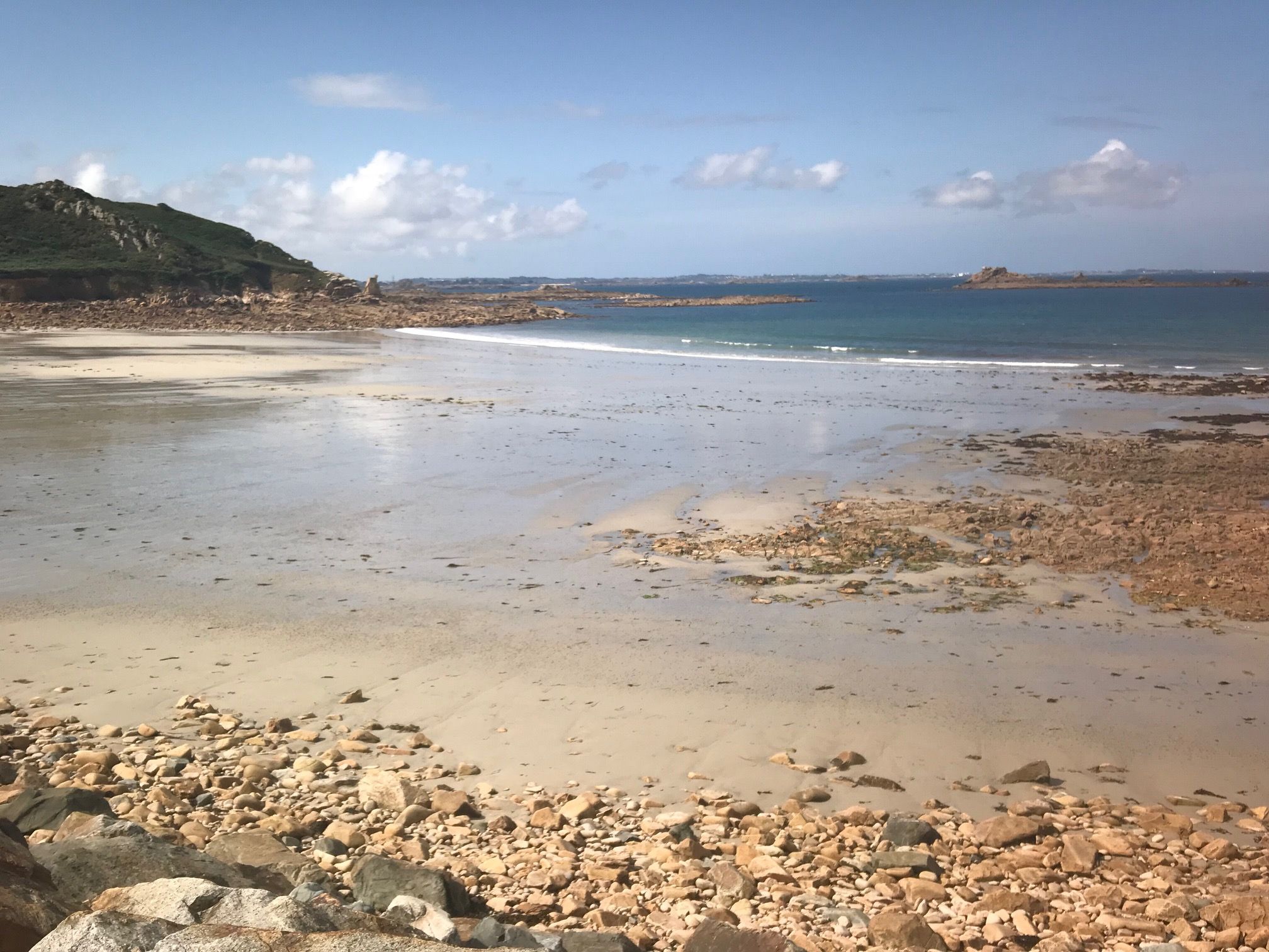 Ein Strand mit felsigem Vordergrund, ruhiger See und weit entfernten Hügeln.