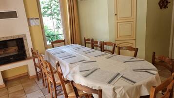 Uma sala de jantar com mesa posta para seis pessoas, rodeada por cadeiras de madeira, lareira e um aparelho de ar condicionado.