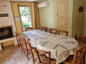 A dining area with a table set for six, surrounded by wooden chairs, a fireplace, and an air conditioning unit.
