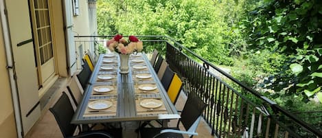 An outdoor dining area with a table set for four, surrounded by chairs, under a shaded pergola.