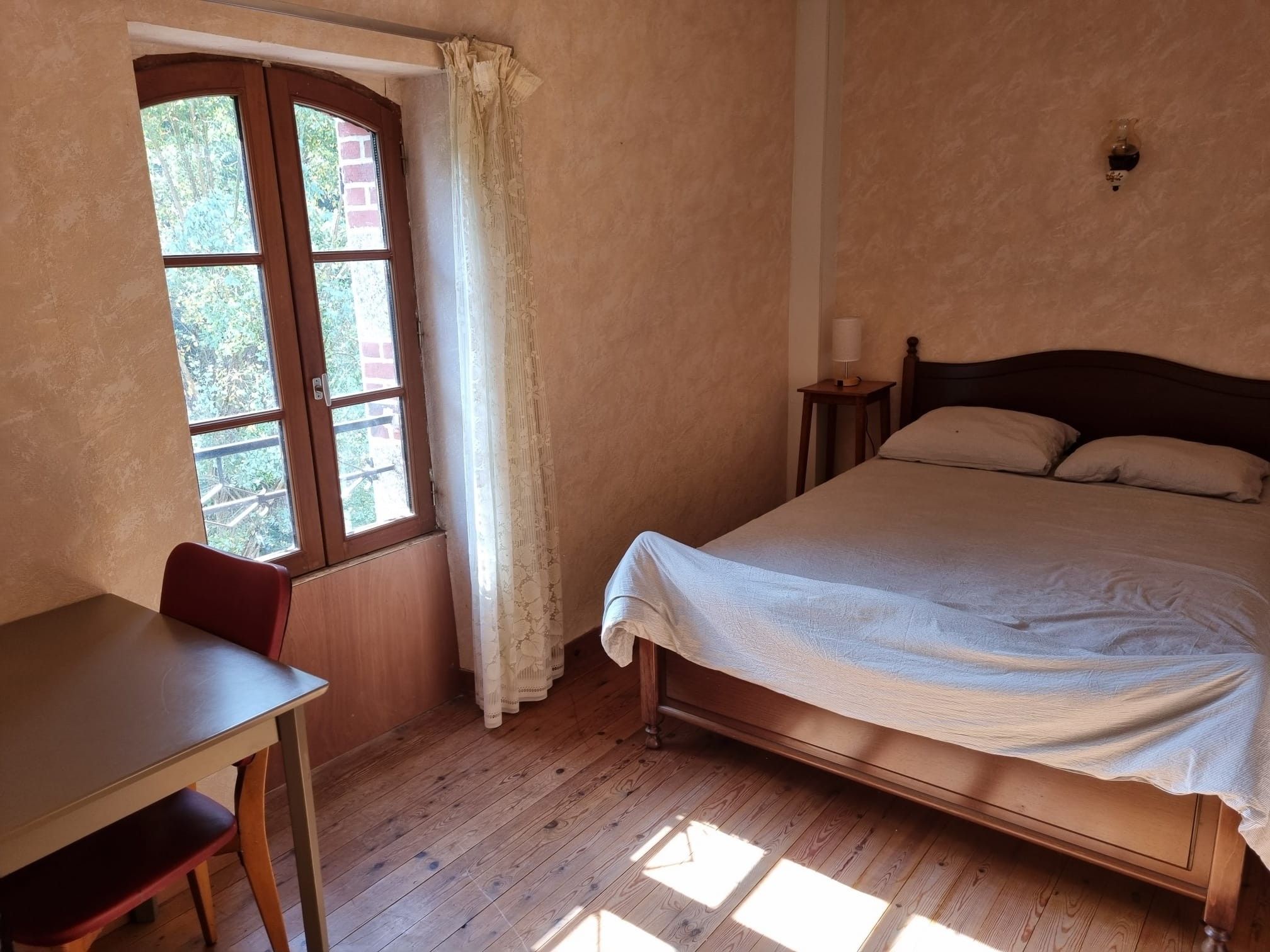 Ein Schlafzimmer mit einem hölzernen Bett, einem kleinen Tisch und einem Fenster mit Vorhängen.