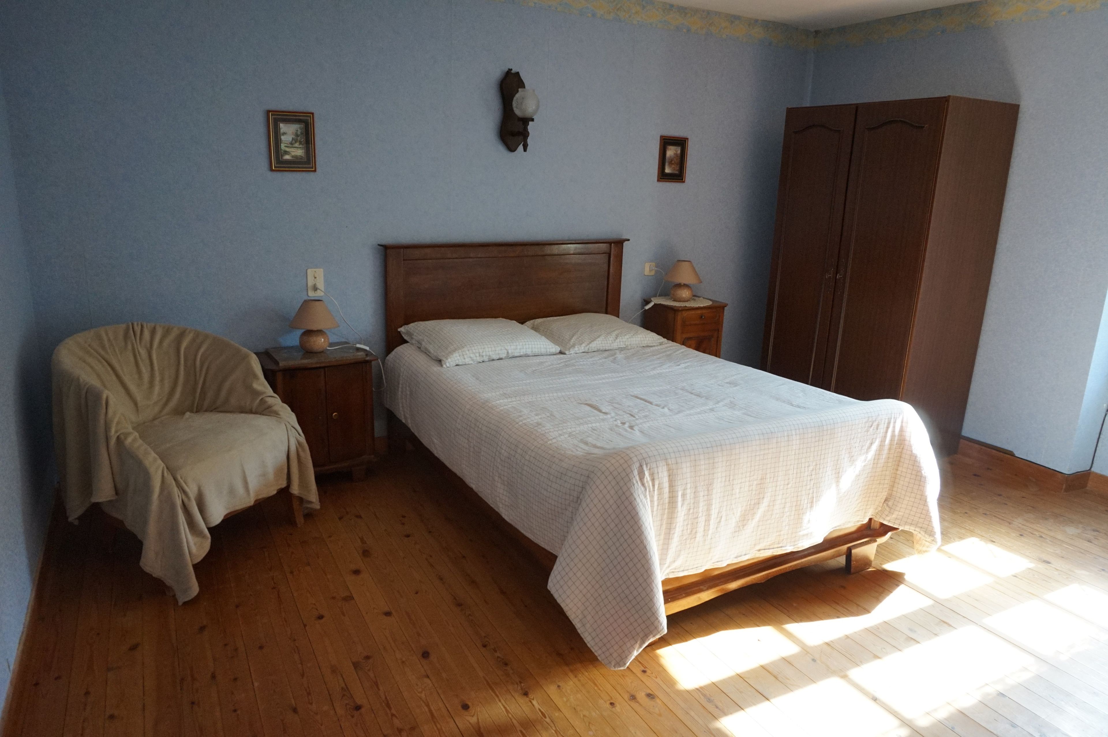 Quarto com cama, uma cadeira, um guarda-roupa e duas mesas de cabeceira.