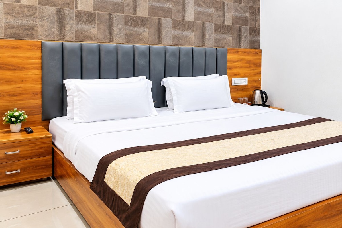 Una cama bien hecha con cabecera de madera, una mesita de noche con lámpara y una pequeña planta en maceta.