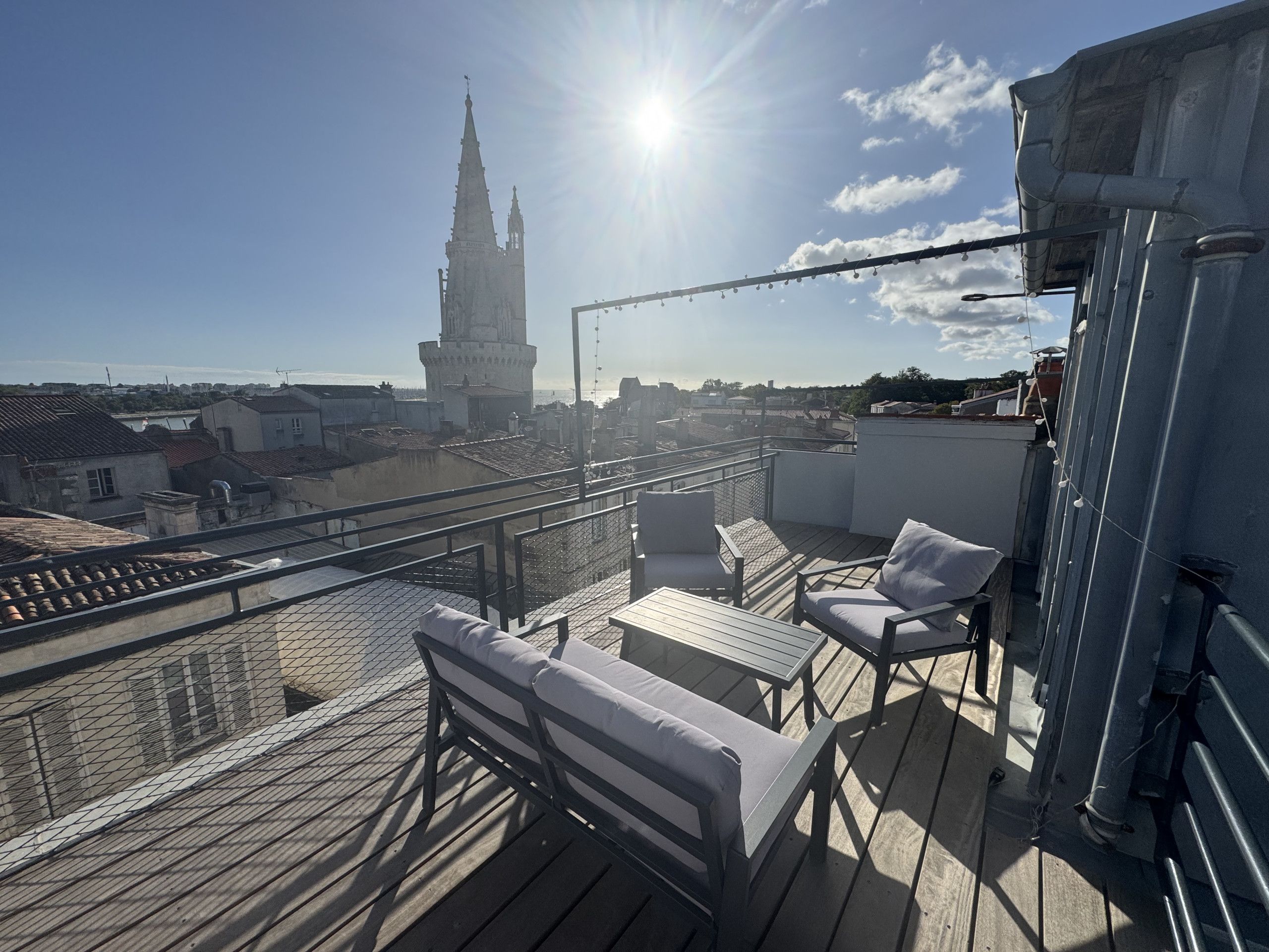 Una terrazza sul tetto con due sedie e un tavolo, con vista su un panorama urbano dominato da un'alta torre.