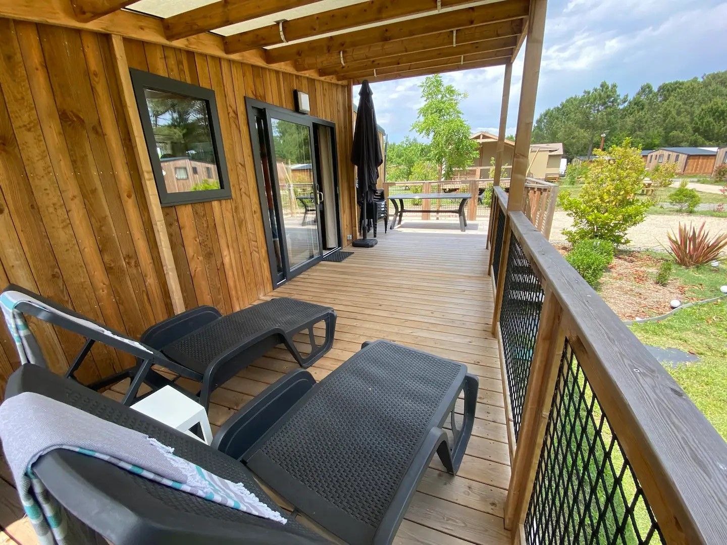 A wooden deck with lounge chairs and a table, overlooking a landscaped garden and residential buildings.