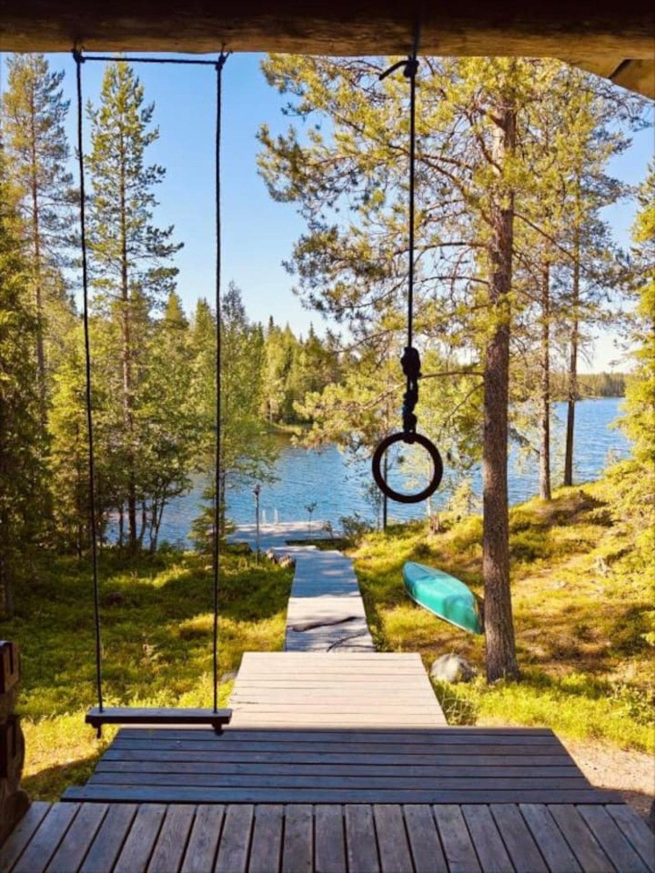 Une terrasse en bois qui mène à un lac, avec une balançoire et un kayak.